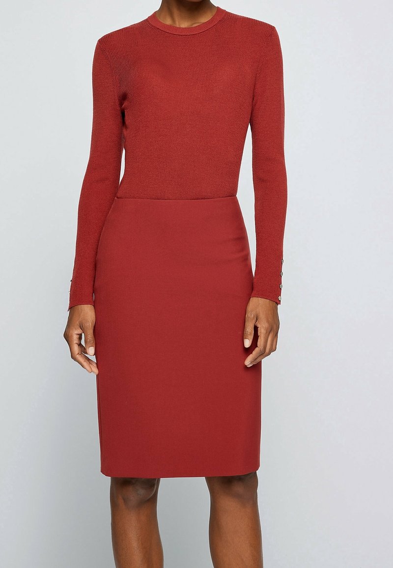 Haut en tricot et jupe crayon ajustée de couleur rouge profond, avec manches longues et boutons décoratifs aux poignets, confectionnés dans un tissu lisse.