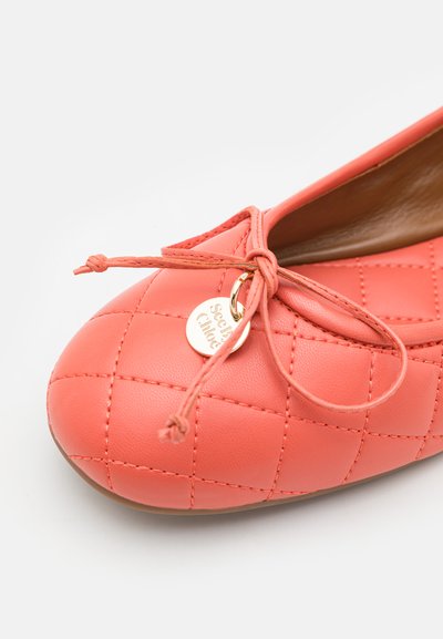 Coral quilted leather ballet flat with a bow and gold round charm on the toe against a white background.