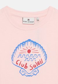 Ανοιχτό ροζ παιδικό πουκάμισο με γραφικό μπλε κοχύλι, έναν κόκκινο ήλιο, κύματα και το κείμενο "Club Soleil" με κόκκινα γράμματα.