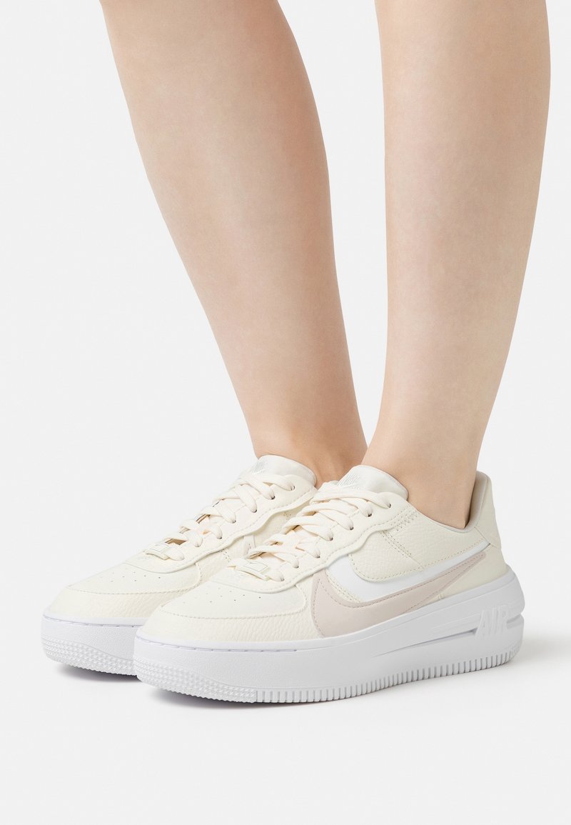 Krémové kožené tenisky s bílou gumovou podrážkou. Mají hladkou texturu, perforovanou špičku a boční akcent v podobě swoosh. Tkaničky jsou v odpovídající barvě.