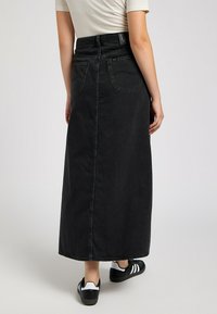 Jupe maxi en denim noire avec une coupe droite, taille haute, poches arrière et un subtil détail de couture, associée à des baskets noir et blanc.