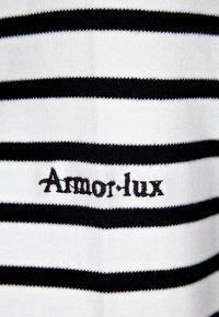 En svart-och-vit randig tyg med en broderad "Armor-lux"-logotyp. Mjuk textur med jämna ränder som framhäver en klassisk nautisk design.
