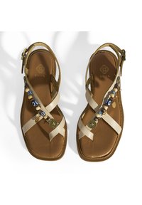 Tan leren sandalen met beige kruisbanden, decoratieve kralen en gouden hardware accenten. Platte zool met stikdetails langs de randen.