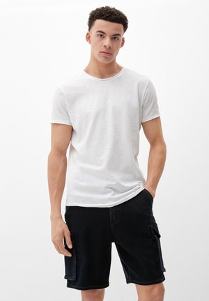 Weißes T-Shirt mit kurzen Ärmeln und leicht strukturiertem Finish, kombiniert mit dunklen Denim-Cargo-Shorts, die seitliche Taschen und eine lockere Passform aufweisen.