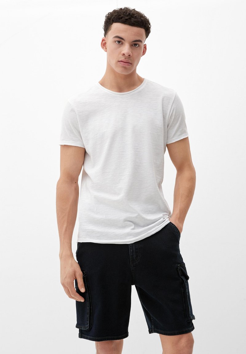 Weißes T-Shirt mit kurzen Ärmeln und leicht strukturiertem Finish, kombiniert mit dunklen Denim-Cargo-Shorts, die seitliche Taschen und eine lockere Passform aufweisen.