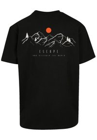 Black cotton t-shirt featuring a mountain design, white outline, and an orange sun. Text reads "ESCAPE AND DISCOVER THE WORLD" in black font.