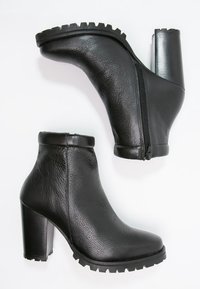 Bottines en cuir noir avec un talon épais, fermeture éclair et finition texturée. Dispose d'une semelle crantée pour une meilleure adhérence et stabilité.