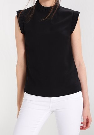 Czarny top bez rękawów z wysokim kołnierzem i falbanami na ramionach, wykonany z gładkiej tkaniny. W połączeniu z białymi spodniami.