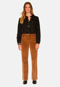 Blouse noire à manches longues avec des d�étails brodés et des boutons, associée à un pantalon en velours côtelé marron évasé et des bottines noires.