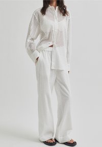 White, grid-patterned, button-up shirt paired with matching wide-leg pants; both feature a lightweight, breathable fabric and loose fit.