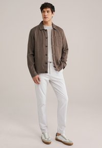 Camisa de botones marrón con un único bolsillo en el pecho, combinada con pantalones blancos y zapatillas gris y blancas. Textura de tela suave.