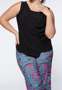 Svart ärmlös topp med draperad framsida, parat med åtsittande leggings med djärva rosa och teal zebraränder. Slät textur, avslappnad stil.