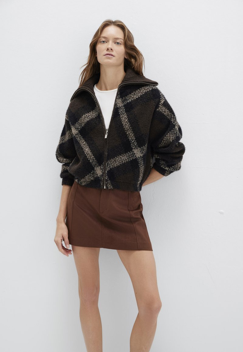 Flauschiger, schwarz-brauner Reißverschluss-Pullover mit Karomuster, kombiniert mit einem figurbetonten, braunen Minirock. Beide Kleidungsstücke haben eine strukturierte Oberfläche.