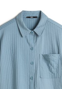Light blue, ribbed shirt with a button-up design, pointed collar, one chest pocket, and light blue buttons. Made from soft fabric.