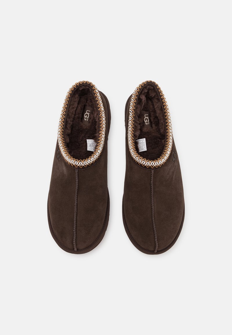 Bruine suède pantoffels met een zachte bontvoering en een decoratieve gevlochten rand rond de opening. Platte zolen voor gebruik binnen.