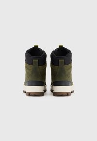 Botine verzi din suede până la gleznă cu guler textil negru, talpă intermediară albă și talpă din cauciuc brun. Previn un tab pentru a fi puse ușor.