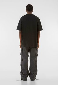 Sort oversized t-shirt med korte ærmer, parret med løstsiddende mørke cargo-bukser med flere sidelommer og justerbare manchetter.