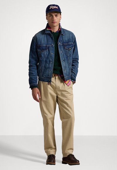 Jeansjakke over en grønn strikkegenser, rutete skjorte, beige bukser og brune sko. Egenskaper inkluderer lommer og en baseballkjole.