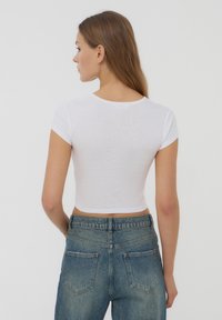 T-shirt bianca cropped con scollo rotondo e maniche corte, abbinata a jeans di denim blu sbiadito a vita alta. Texture liscia.