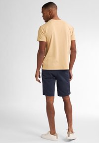 Tricou din bumbac bej deschis cu mâneci scurte, asortat cu pantaloni scurți bleumarin și adidași bej. Design simplu cu guler rotund.