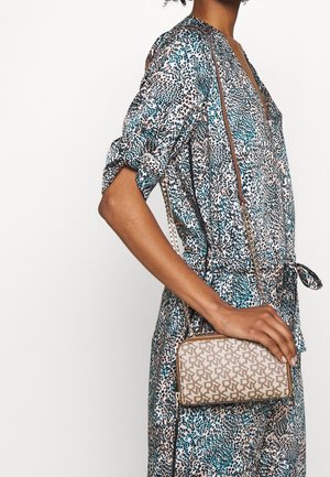 Bolso beige texturizado con un patrón geométrico, con una correa de cadena dorada. El fondo muestra un conjunto con estampado de leopardo multicolor.