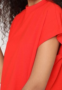 Haut rouge à manches courtes avec un col montant et une coupe décontractée. Le tissu semble doux, avec une texture subtile et des détails de couture minimalistes.