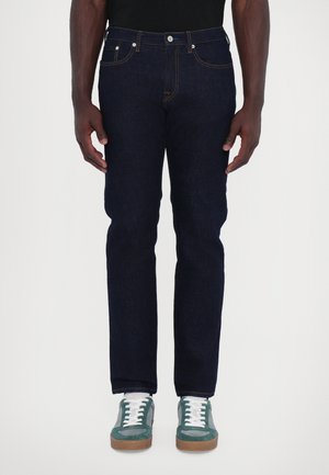 Dark blue denim jeans with a straight fit, featuring a classic five-pocket design and stitched accents. Paired with teal sneakers.