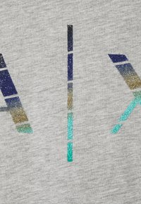 Grått tyg med en texturerad, glittrig logotyp som har blå, gröna och gyllene gradientmönster arrangerade i geometriska former.