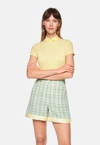 Yellow polo shirt with a classic collar paired with check-patterned shorts in pastel colors. The shorts feature a contrasting yellow hem.