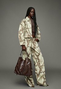 Geknipte, gemarmerde blazer en broek in gedempt groen en bruin, gecombineerd met een grote bruin leren handtas met gestructureerde accenten en hardwaren.