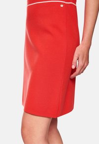 Roter, eng anliegender Rock aus weichem Material, mit einer weißen horizontalen Linie nahe der Taille und einem kleinen silbernen Akzent an der Seite.