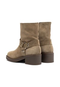 Botas de tobillo de ante marrón con puntera redondeada, correa decorativa y detalles de metal en tono plateado, y un tacón bajo rectangular para mayor estabilidad.