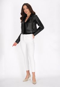 Giacca da biker in pelle sintetica nera con tasche con zip, jeans bianchi a vita alta e tacchi a punta beige.