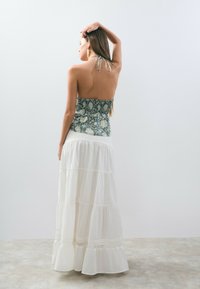 Vestido maxi con un cuerpo de patrón floral en azul y blanco, que transiciona a una falda blanca en capas. Presenta un escote halter y una cintura fruncida.
