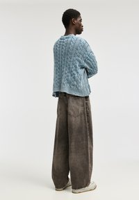 Välj raka, ljusblå kabelstickade tröjor med ribbat avslut och sänkta axlar, i kombination med mörkgrå vida jeans och vita sneakers.