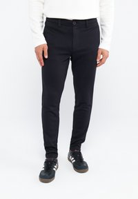 Zwarte slim-fit chinos met een gladde textuur, voorzien van een knoopsluiting en zijzakken, gecombineerd met zwart en marineblauwe sportschoenen.