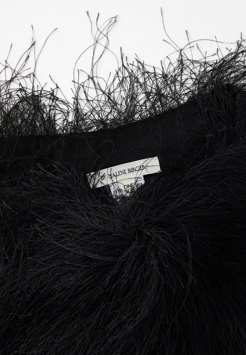 Borde negro texturizado de plumas en la tela que muestra la etiqueta de la prenda "By Malene Birger" en texto negro claro sobre una etiqueta blanca.