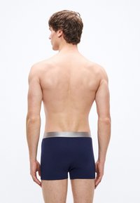 Calzoncillos bóxer azul marino con una cintura elástica plateada. Tela suave con textura lisa, diseño ceñido que cubre la zona superior del muslo.