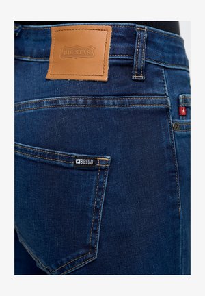 Jeans de mezclilla azul oscuro con un parche de cuero etiquetado "BIG STAR" en la cintura, que presenta una pequeña etiqueta negra en el bolsillo trasero.