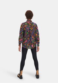 Kleurrijke lange mouwen shirt met een bloemen- en paisleyprint, met een zwarte achtergrond. Gecombineerd met zwarte leggings en bruine enkellaarzen.