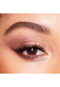 Close-up of a brown eye with dark eyelashes, soft copper eyeshadow, and well-defined eyebrow. Skin texture appears smooth and even.