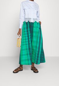 Vaaleansininen lyhyt paita, jossa on pitsireunus, yhdistetty vihreään ruudulliseen hameeseen. Mustat remmisaappaat ja pieni keltainen ruudullinen laukku.