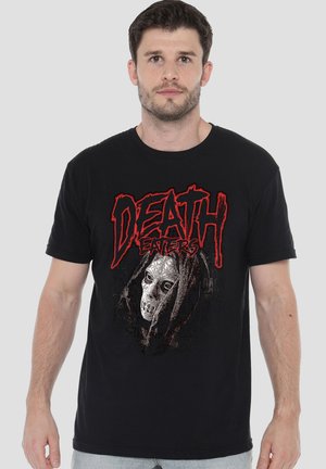 Mann mit kurzem dunklem Haar, der ein schwarzes T-Shirt mit rotem "Death Eaters"-Text und einer detaillierten weißen Maskengrafik auf der Vorderseite trägt.