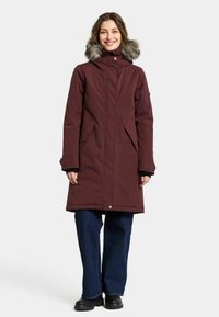 Bordeaux parka med en hætte i pels, lynlåslommer og en længere pasform. Har en glat tekstur og et holdbart stof. Båret med mørke jeans.
