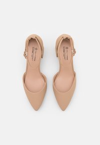 Beige-kärjiset korkokengät, joissa on sileä mattapinta, matala lohkokorko ja säädettävä nilkkavyö. Sisällä on pehmeä, pehmustettu pohja.