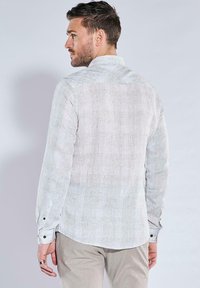 Weißes Hemd mit langen Ärmeln, aus strukturiertem Stoff mit einem dezenten Muster, ausgestattet mit einer Rückenpasse und knöpfbaren Manschetten.
