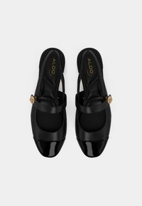 Black slingback shoes featuring a matte leather upper, shiny patent toe cap, and a gold circular embellishment on the strap.