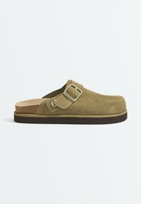 Sabot en daim vert olive à enfiler avec semelle intérieure en liège, bride réglable à boucle métallique, et semelle extérieure en caoutchouc marron foncé.