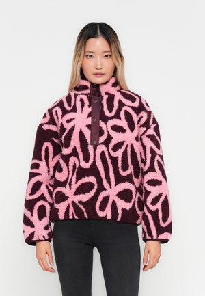 Fleece pullover in donker bourgondië met roze bloemenpatronen, hoge kraag en drukknoopsluiting. Zacht, gestructureerd materiaal met een oversized pasvorm.