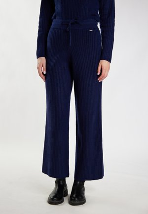 Femme portant un pantalon large en maille côtelée bleu marine avec taille à cordon et bottines en cuir noir.